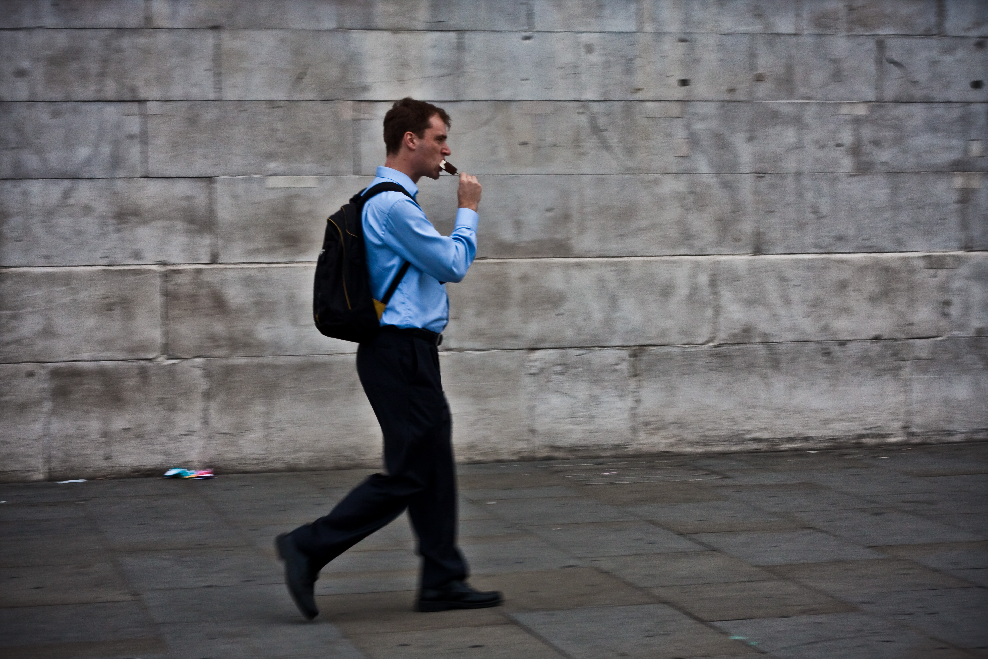 A man eats a chocolate ice lolly while walking past the wall.